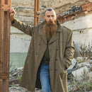 Man wearing a khaki vintage Italian military trench coat with double-breasted buttons and belt, outdoors.