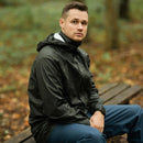 Man wearing black waterproof rain jacket with hood sitting on wooden bench in forest setting