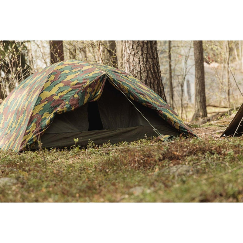 Genuine Belgian military two-person waterproof tent set up in forest with ripstop camouflage fabric and sturdy poles.