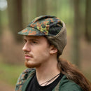 Man wearing genuine German Army flecktarn winter pile cap with ear flaps and faux fur lining in forest setting