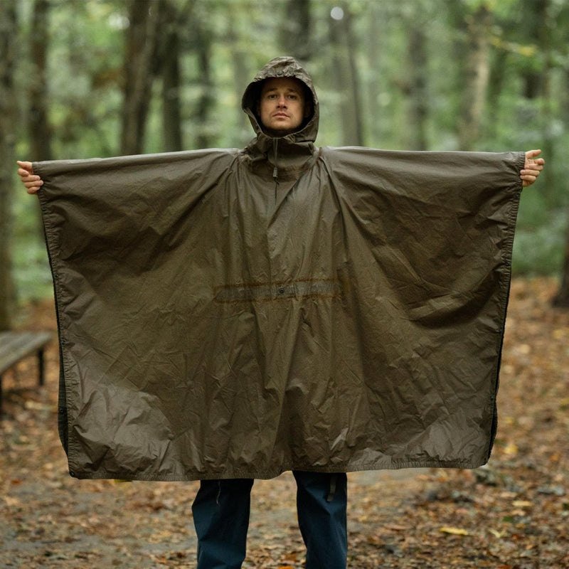 Man wearing vintage German army waterproof olive green rain poncho with hood standing in forest