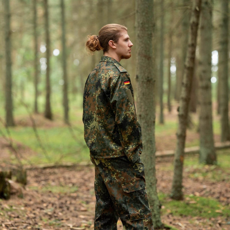Man wearing Leo Kohler flecktarn camouflage tactical military shirt and pants standing in forest background