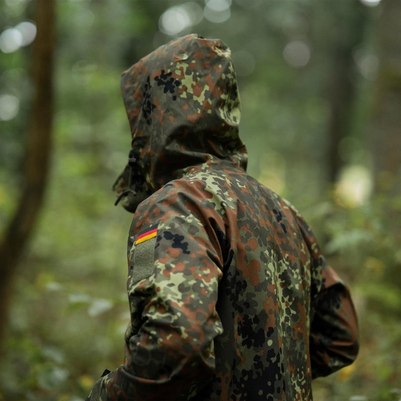 Person wearing Mil-Tec German army field jacket in GoreTex Flecktarn camo in forest setting, waterproof rain protection