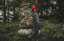 Person hiking in forest wearing large camo Belgium military tactical backpack with rolled sleeping mat attached