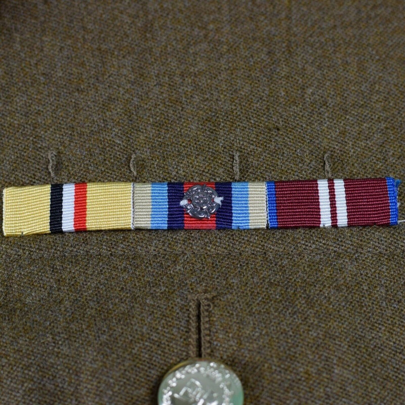 Close-up of British military uniform medal ribbons on a khaki fabric background with a metal button below.