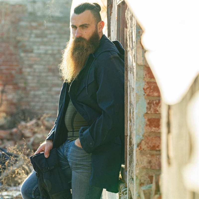 Man wearing original Dutch military officer parka in solid blue leaning against a brick wall outdoors