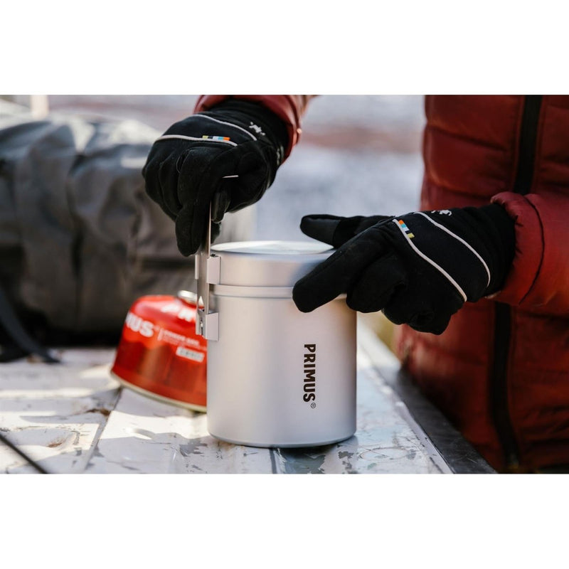 Person wearing gloves opening compact Primus Essential Trek Pot lightweight 1-liter camping cook set outdoors