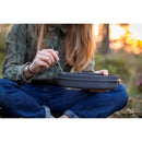 Person holding Primus Frigg W Piezo mess kit camping meal set while sitting outdoors at sunset