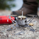 Compact Primus MultiFuel III hiking stove with high-output burner on rocky ground for outdoor camping use