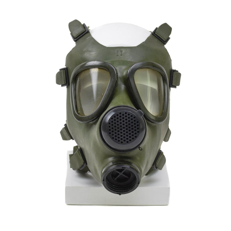 Vintage Romanian M74 full face NBC gas mask in olive green with dual eyepieces and exhale valve displayed on white stand.